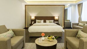 Una habitación de hotel con una cama grande, dos mesitas de noche, una mesa de centro con un jarrón de flores y dos sillones.