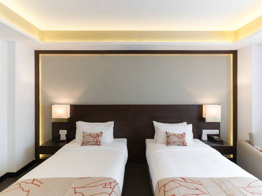 A hotel room with two single beds, nightstands with lamps, a headboard, and a chair.