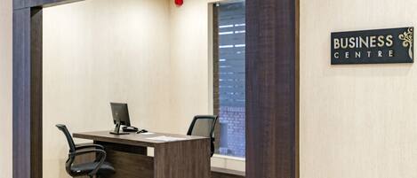 A business center with a wooden desk, two black office chairs, and a computer. A sign on the wall reads "BUSINESS CENTRE".