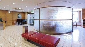 Zona de recepción con un banco rojo, un piano y una gran pared cilíndrica con texto.