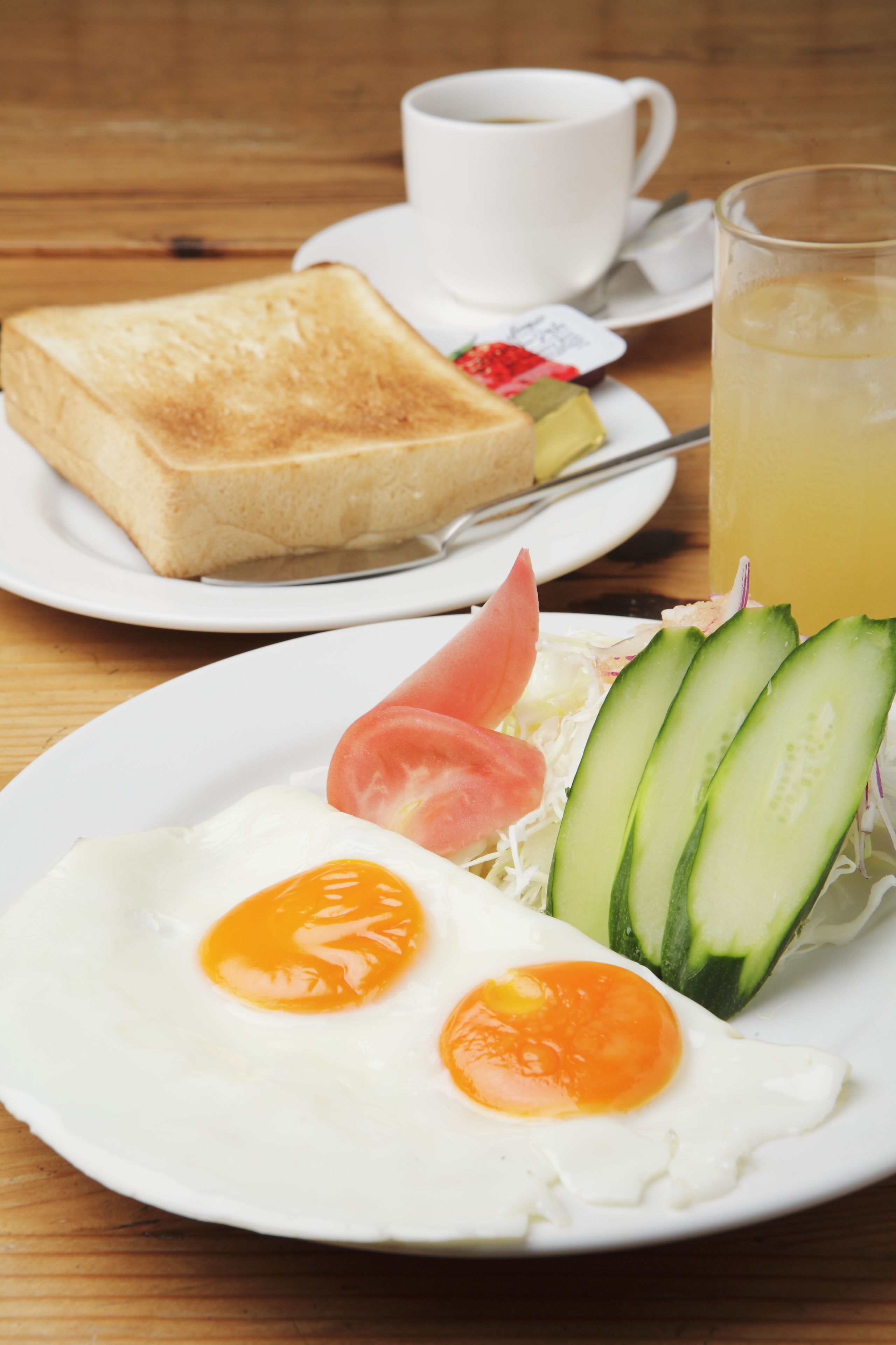 Un plato de desayuno con tostadas, huevos, pepino, tomate y un vaso de jugo de naranja.