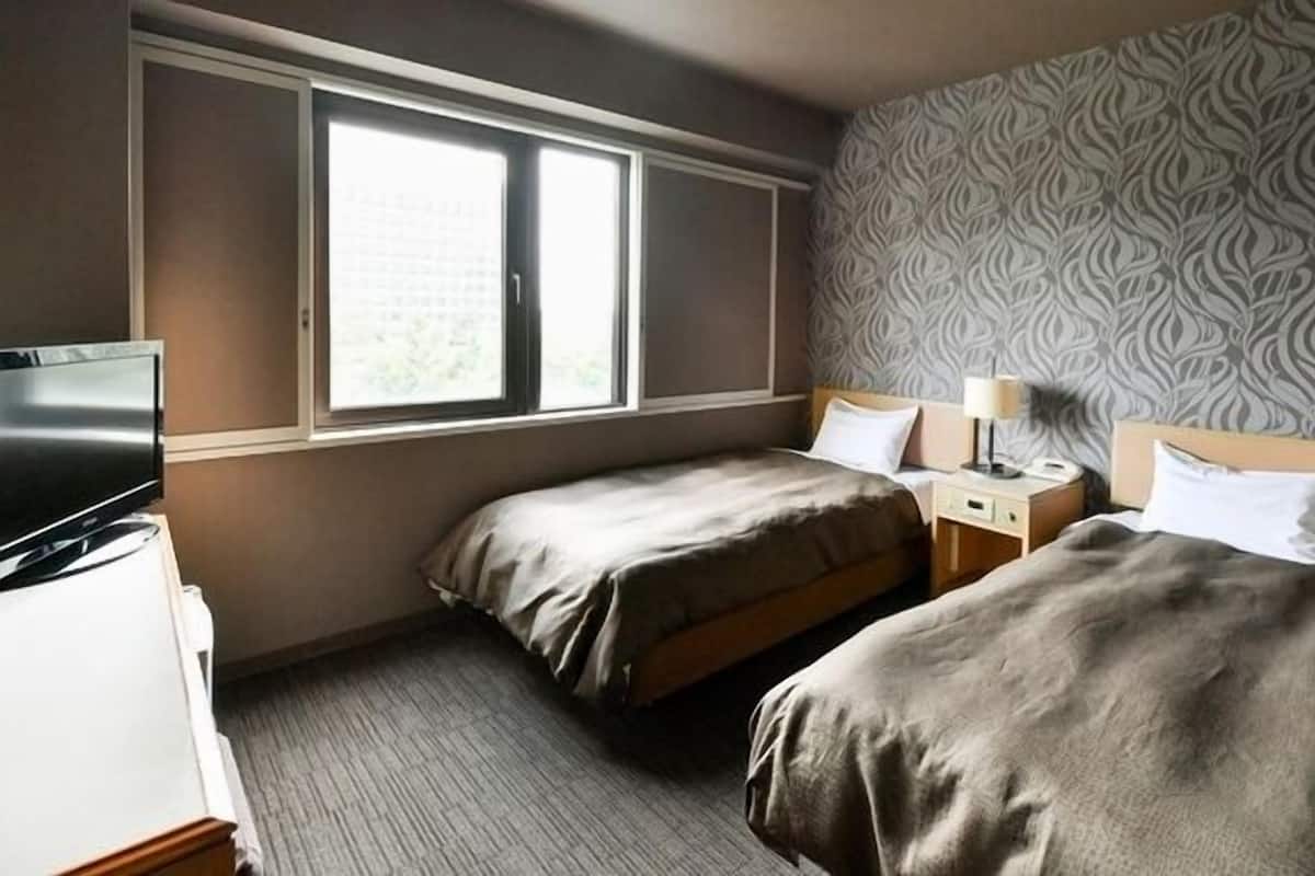 Ett hotellrum med två separata sängar, en TV, ett nattduksbord med en lampa och en vägg med ett mönster.
