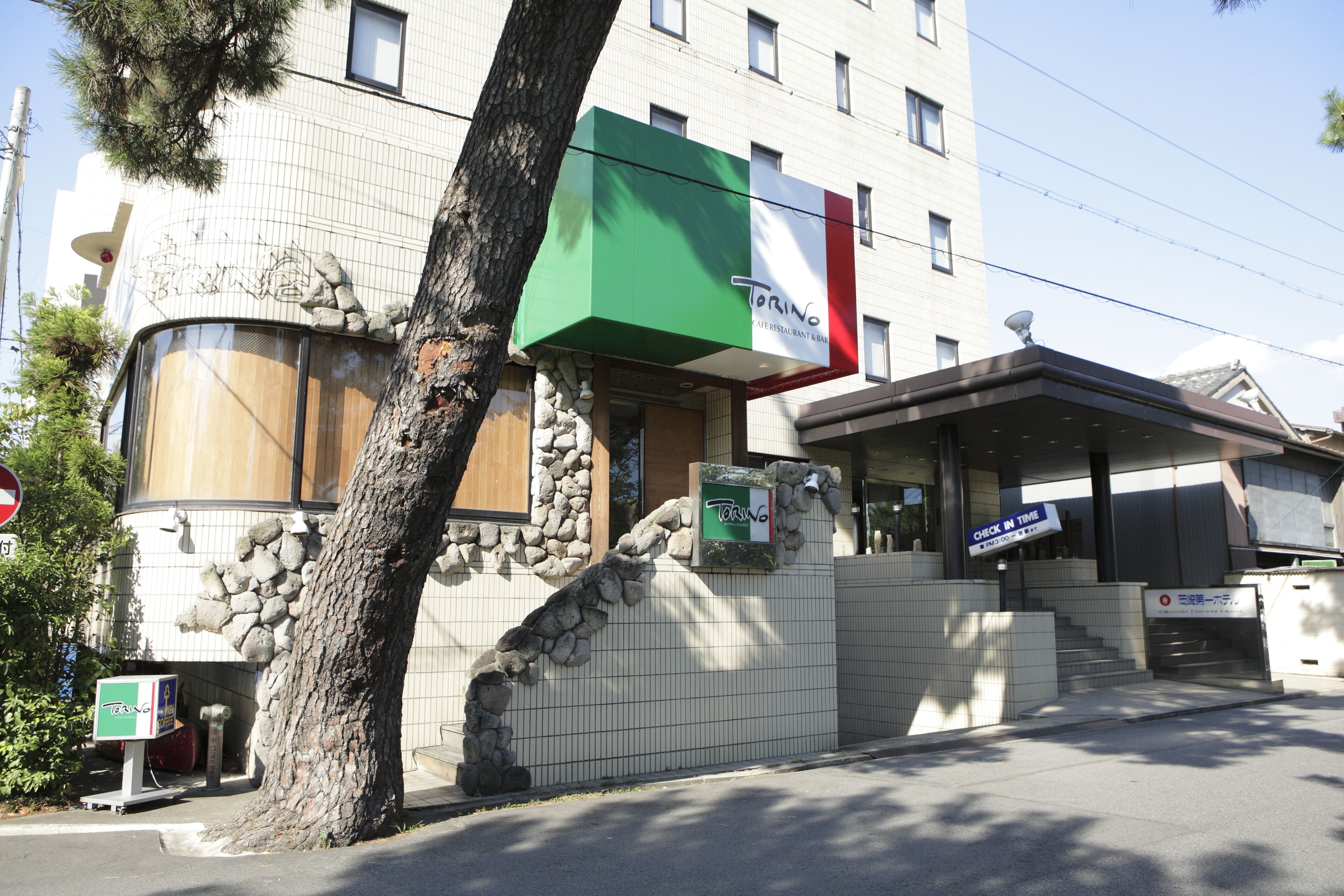 A building with a restaurant sign, stone wall, and a tree in front.