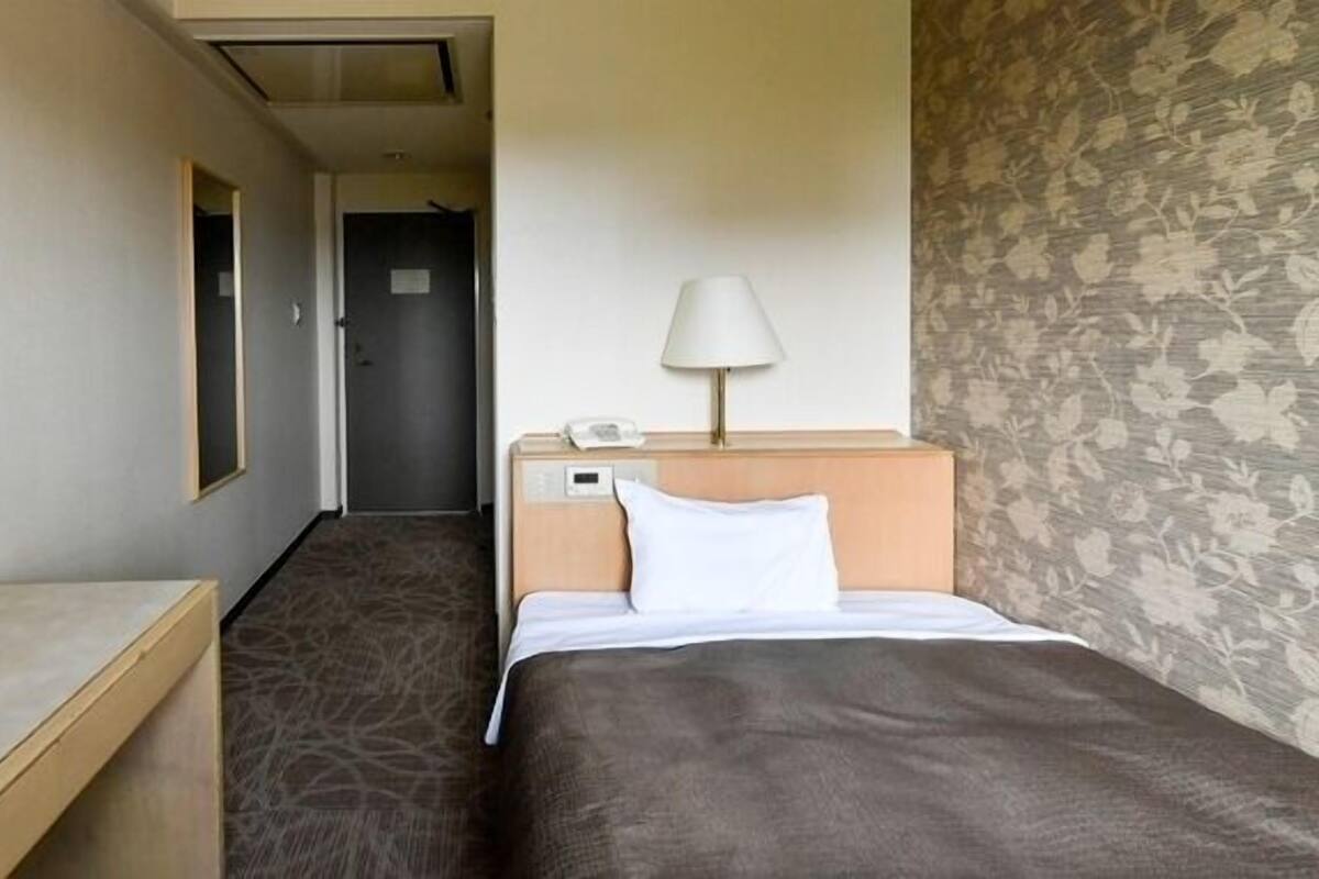 Ett hotellrum med en säng, ett sängbord, en lampa och en telefon.