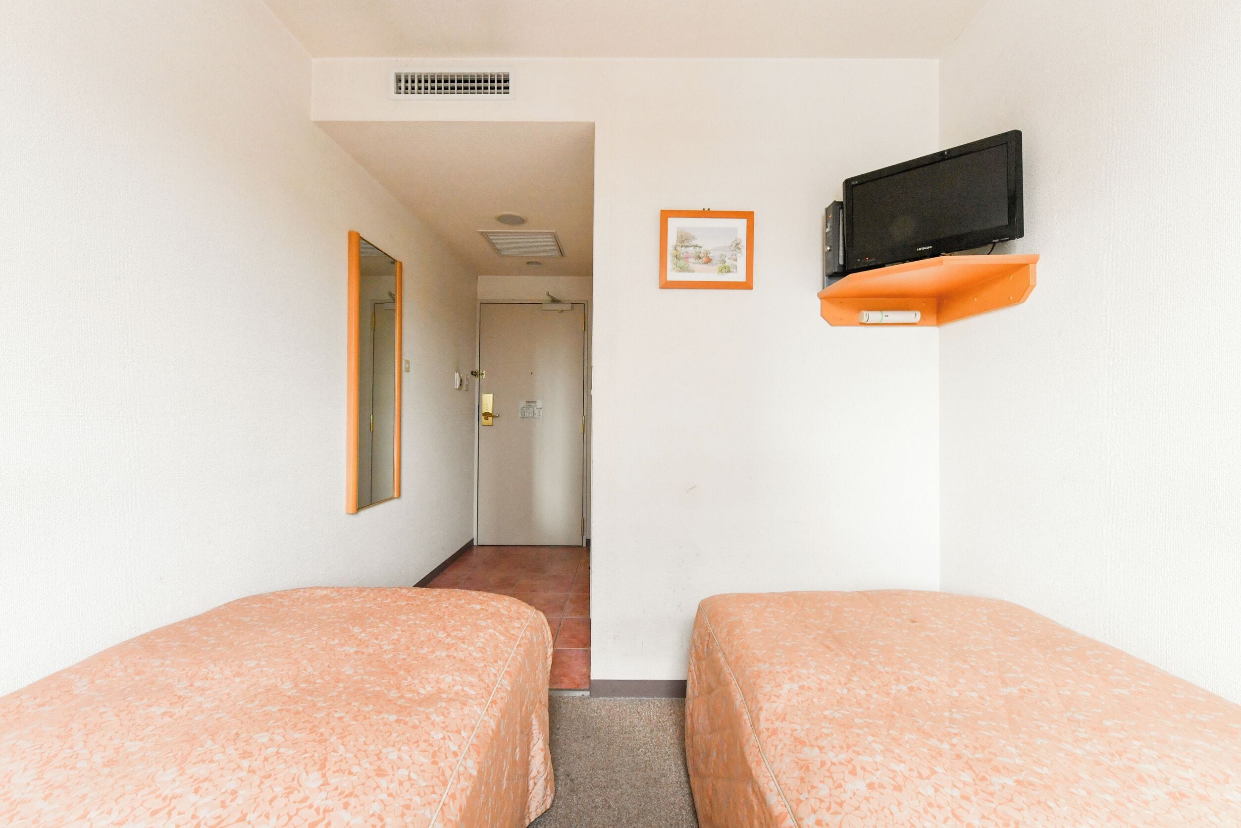 A hotel room with two beds, a television on an orange stand, a framed picture on the wall, and a door leading to a bathroom.