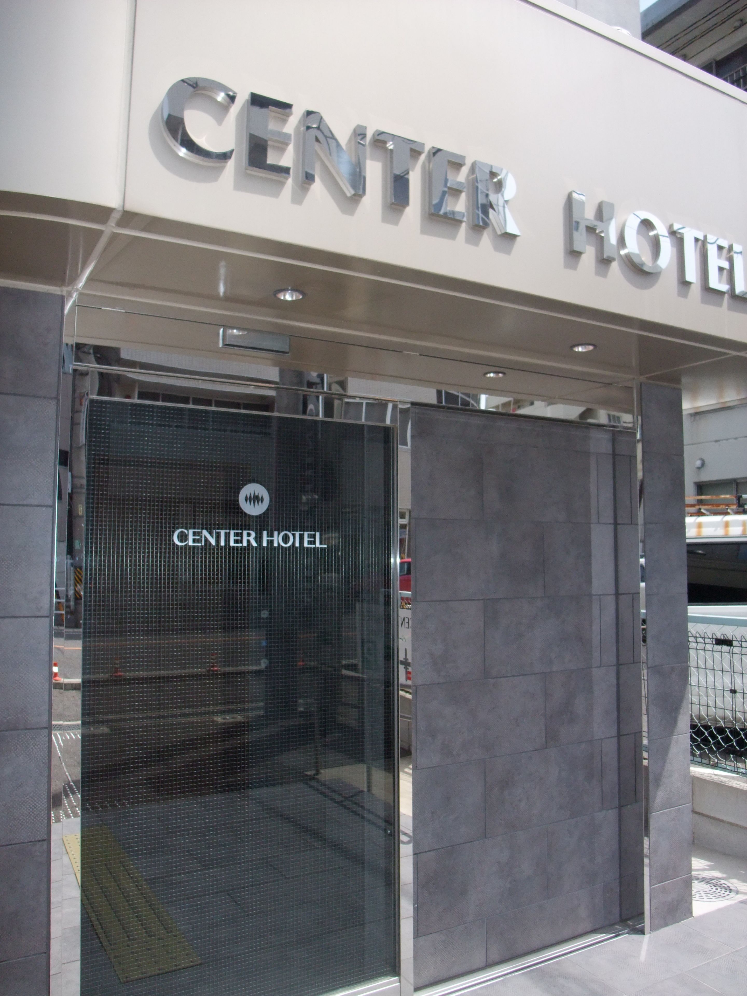 La entrada del Centro Hotel, con puerta de vidrio y estructura metálica.