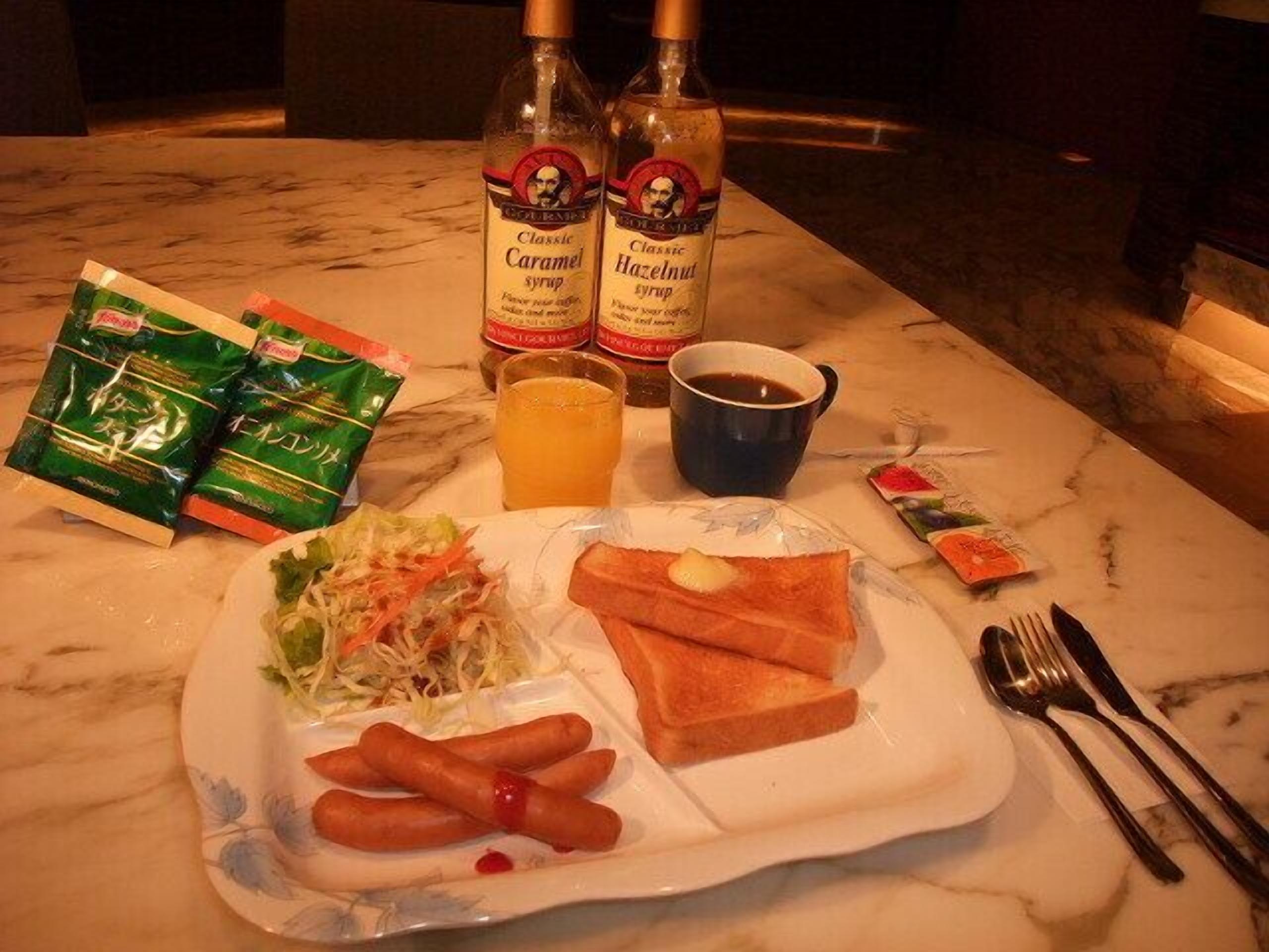 A meal with sausages, toast, salad, and condiments on a marble table.