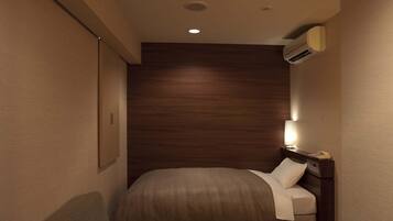 A compact hotel room with a single bed, a bedside table with a lamp, and a small seating area.