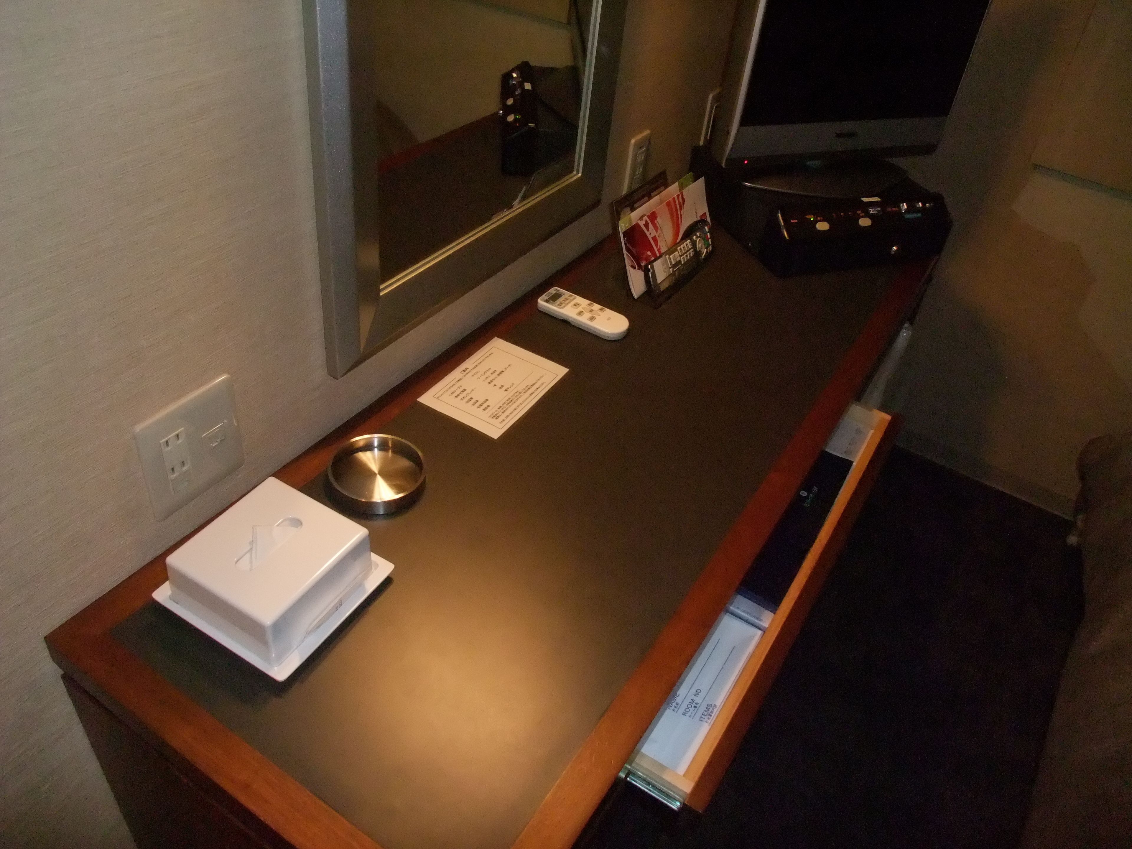 A hotel room counter with a microwave, a remote control, a menu, a tray, and a drawer.