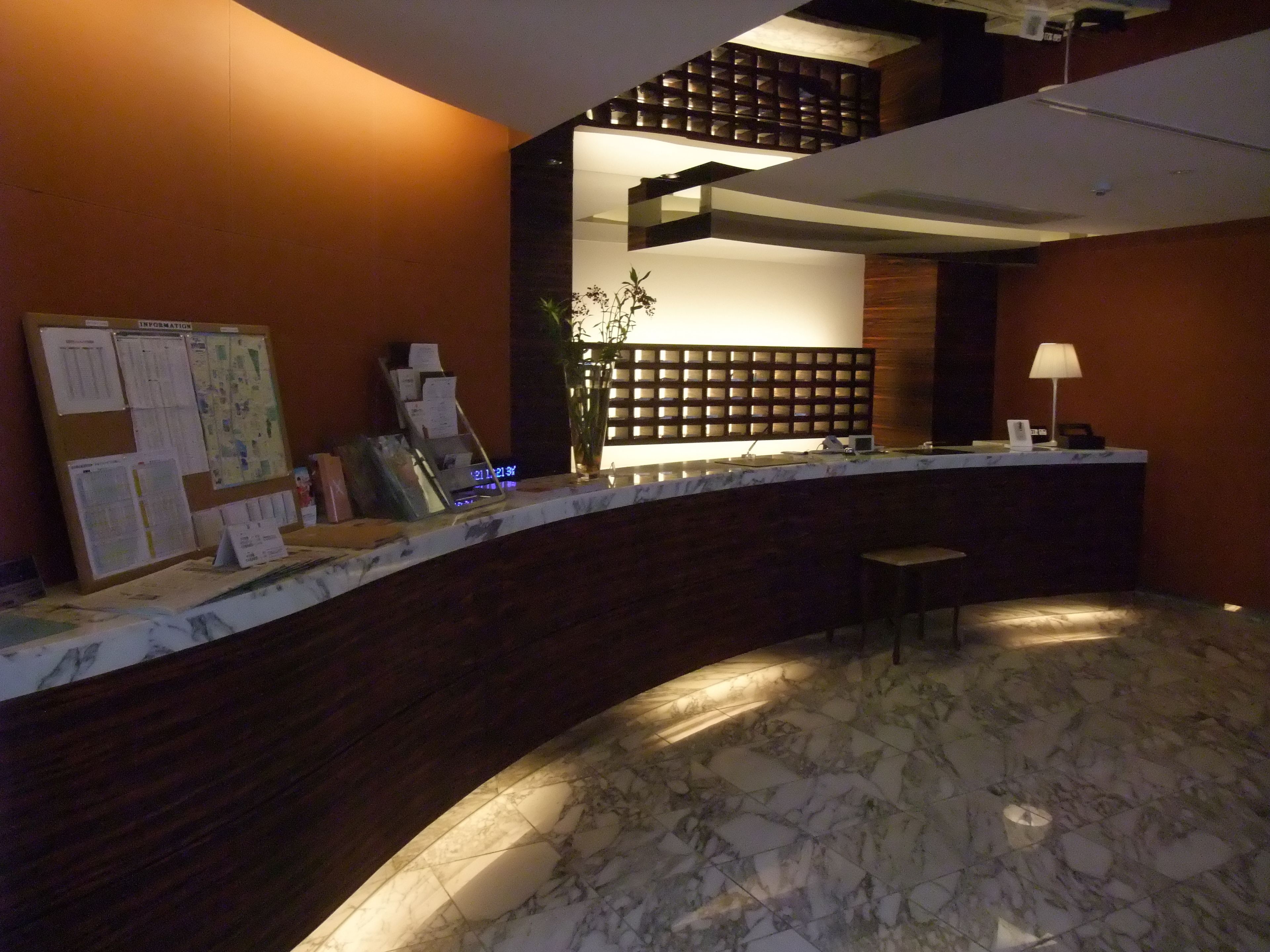 Zona de recepción con piso de mármol, mostrador de madera y un tablón de anuncios con documentos.