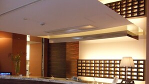 Uma área de recepção moderna com balcão de mármore, painéis de madeira e um banco para acomodação.