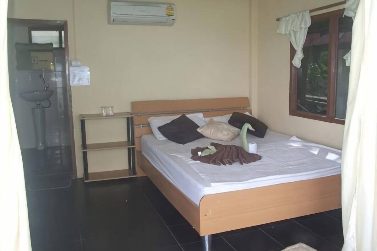 A bedroom with a bed, a bedside table, a window, and a wall-mounted air conditioner.