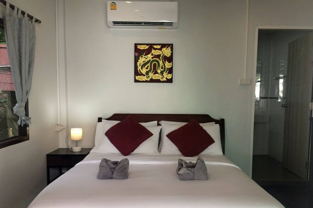 A neatly made bed with two pillows, a wall-mounted air conditioner, and a decorative piece above the bed.