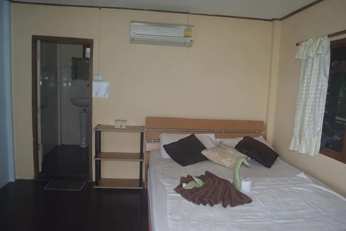 A hotel room with a bed, a bedside table, a mirror, an air conditioning unit, and a window with curtains.