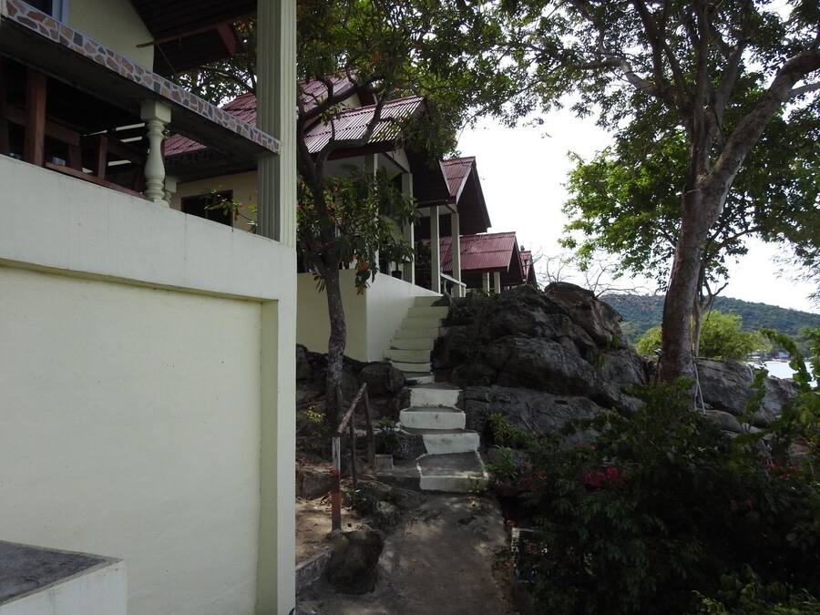 A staircase leading to a building with a red roof, surrounded by greenery and overlooking a body of water.