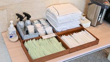 A hotel reception area with a wooden counter, a stack of white towels, a hand sanitizer dispenser, a tissue box, and a waste bin.