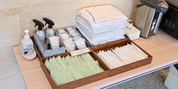 A hotel reception area with a wooden counter, a stack of white towels, a hand sanitizer dispenser, a tissue box, and a waste bin.