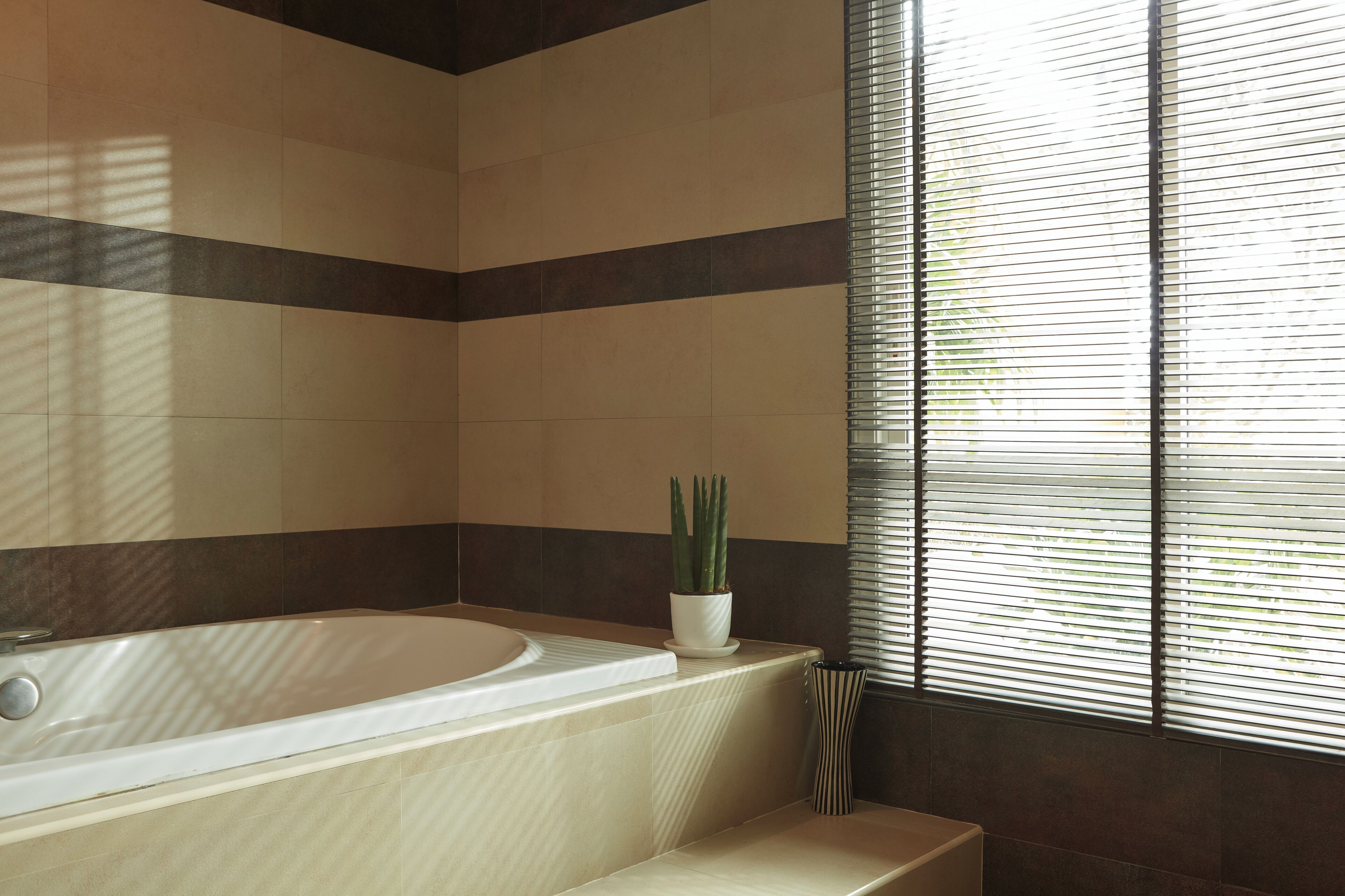 Une salle de bain avec une baignoire, une plante en pot et une fenêtre avec des stores.