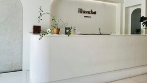 A hotel reception desk with a modern design, a sign that reads "Rhionchai Hotel," and a potted plant on the counter. - Rhienchai Place (Surat Thani)