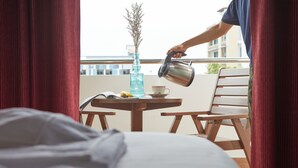 A person pouring water into a cup on a balcony table with a book, a banana, and a vase of flowers. - Rhienchai Place (Surat Thani)
