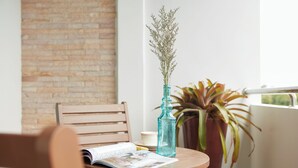A wooden chair with a magazine, a blue vase with dried flowers, and a potted plant on a round table. - Rhienchai Place (Surat Thani)