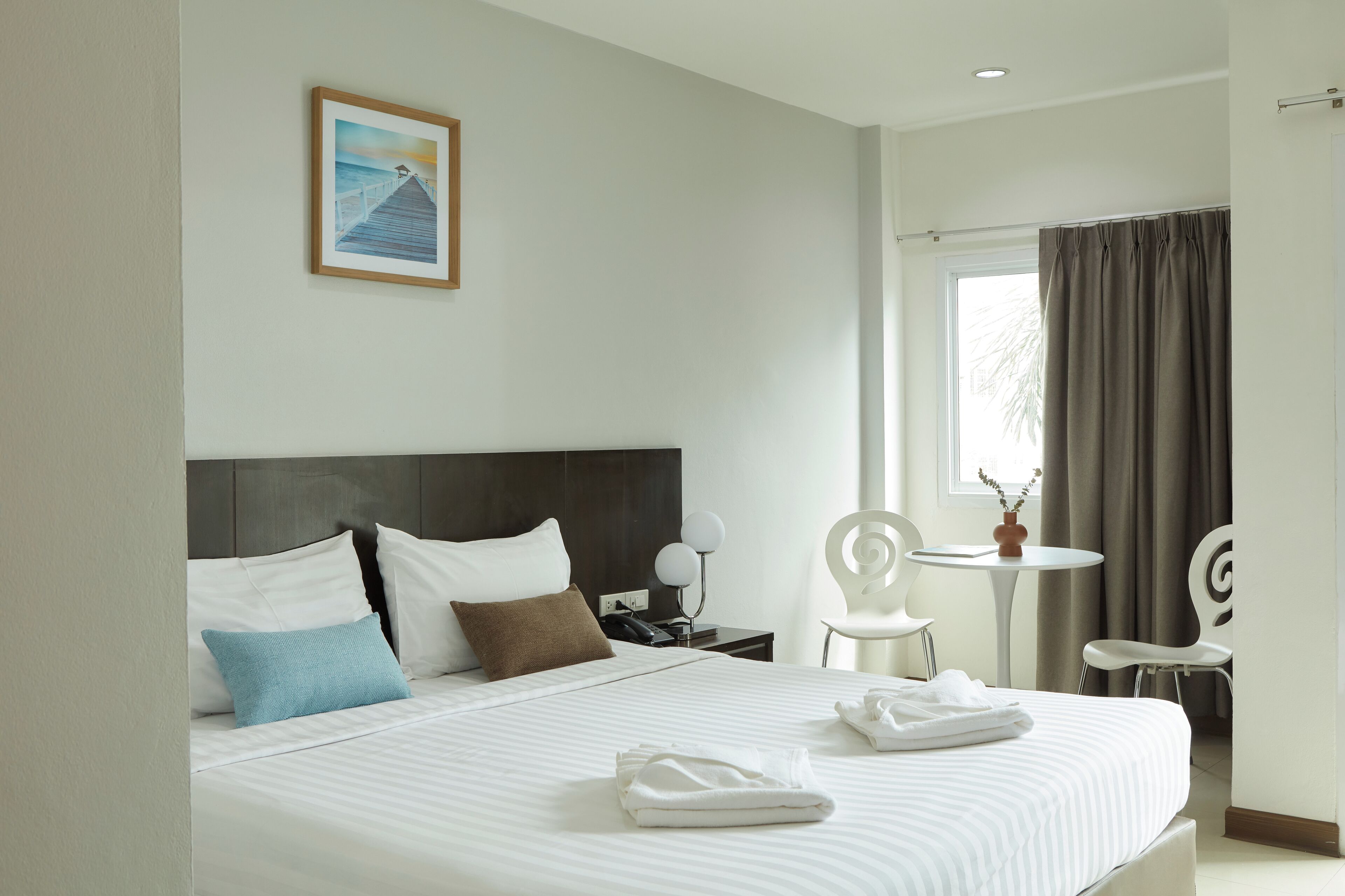 A hotel room with a large bed, a nightstand, a desk, two chairs, and a window with curtains.