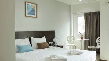 A hotel room with a large bed, a nightstand, a desk, two chairs, and a window with curtains.