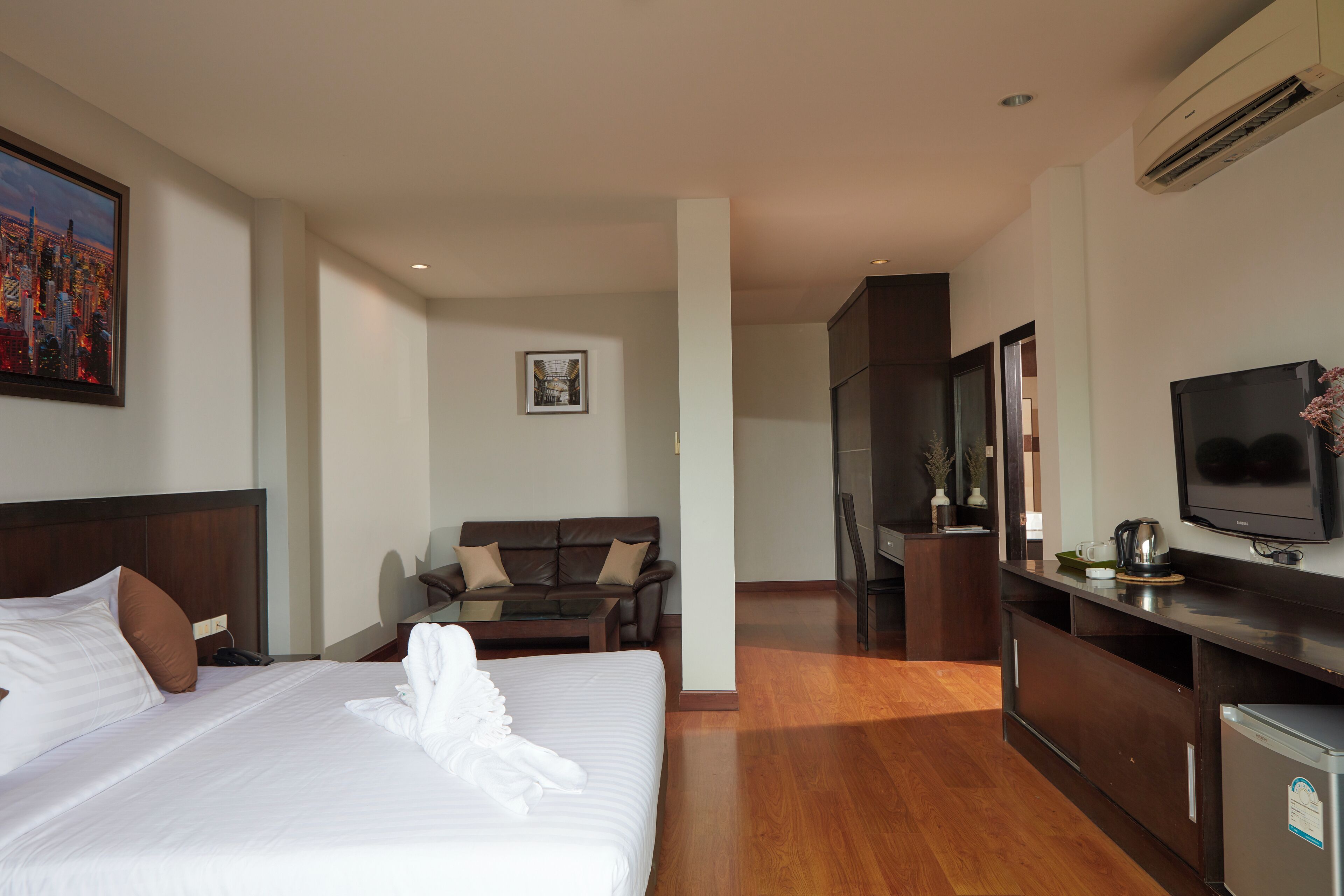 A hotel room with a large bed, a sofa, a television, and a kitchenette.