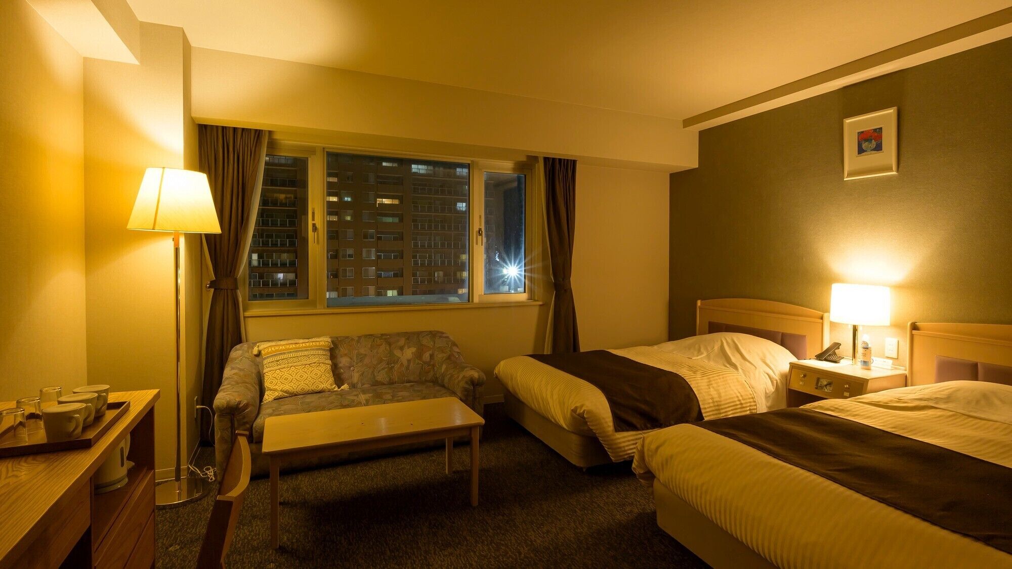 A hotel room with two beds, a sofa, a table, and a lamp.