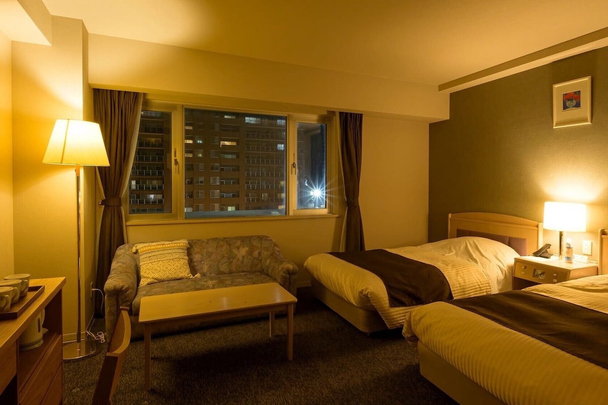 A hotel room with two beds, a sofa, a table, and a lamp.