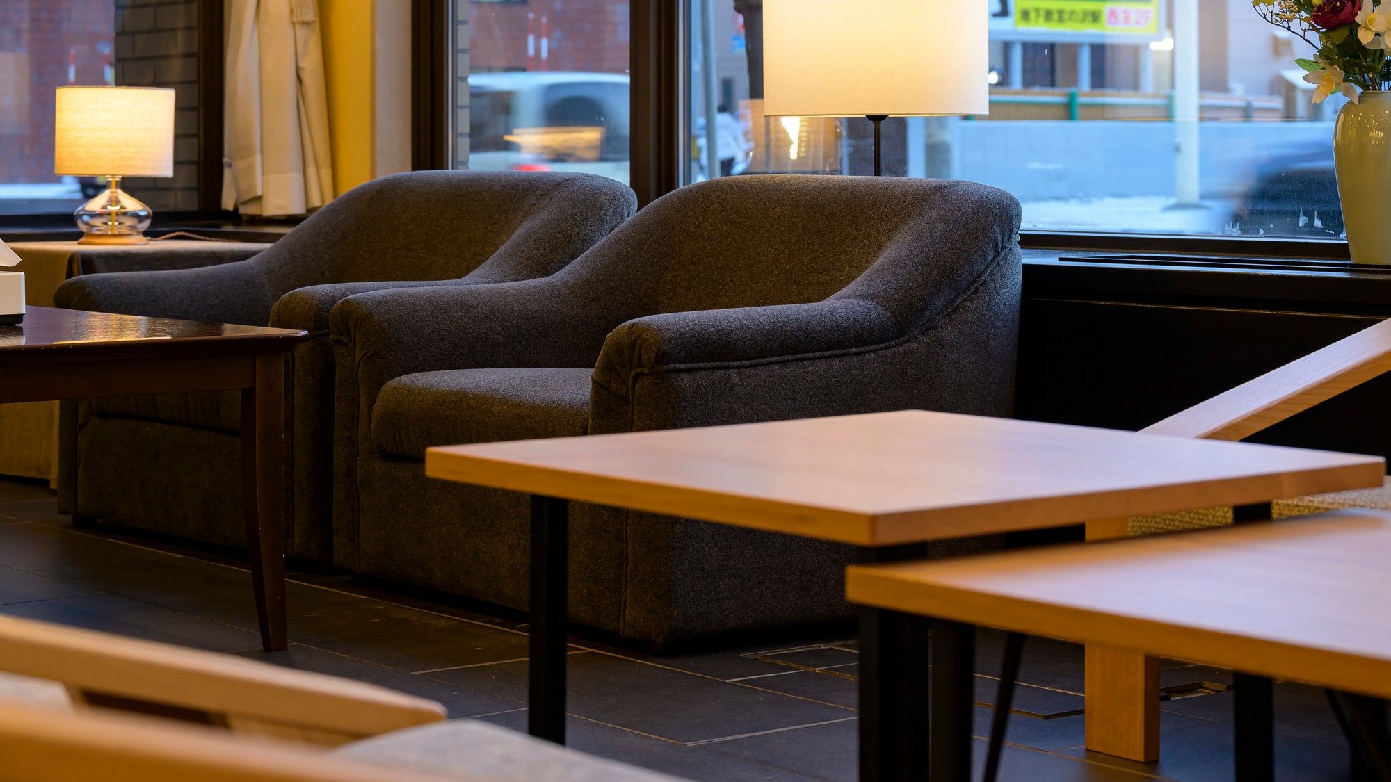 Un coin salon avec deux fauteuils et une table, une lampe, et une vue sur la rue par une fenêtre.