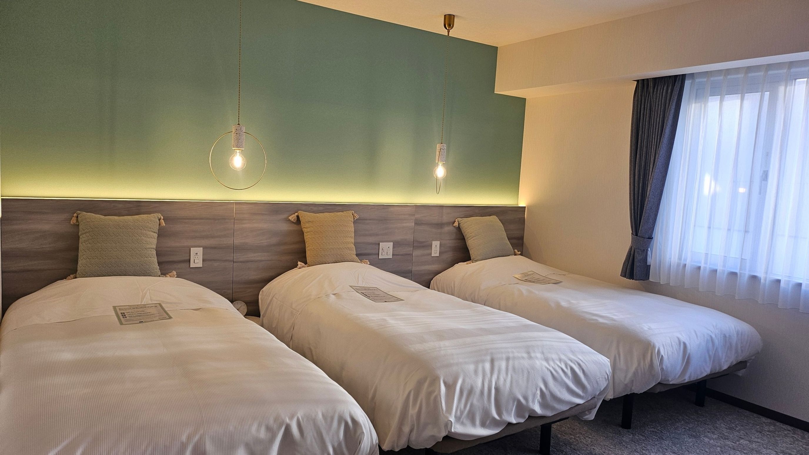 A hotel room with two single beds, a wooden headboard, and a large window with curtains.