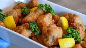 A dish of fried chicken with broccoli and lemon wedges.