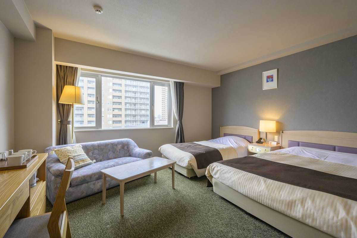A hotel room with two beds, a sofa, a desk, and a window with curtains.