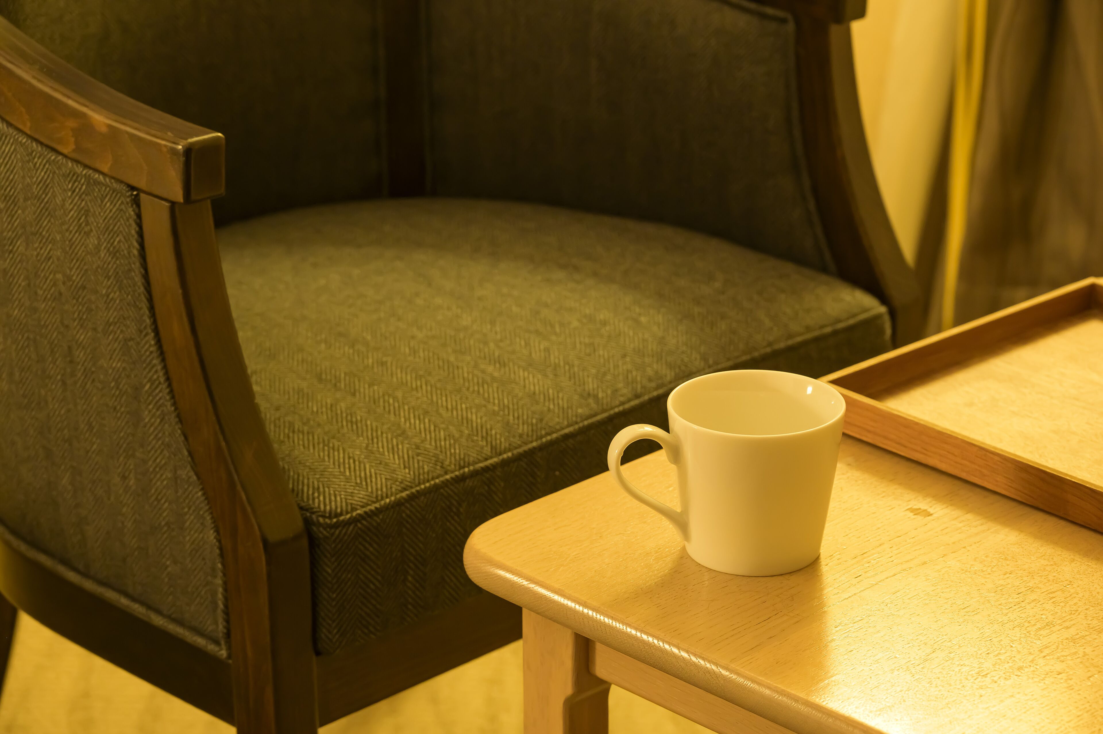 A wooden chair with a cushioned seat and backrest, a white mug on a wooden tray, and a wooden table.