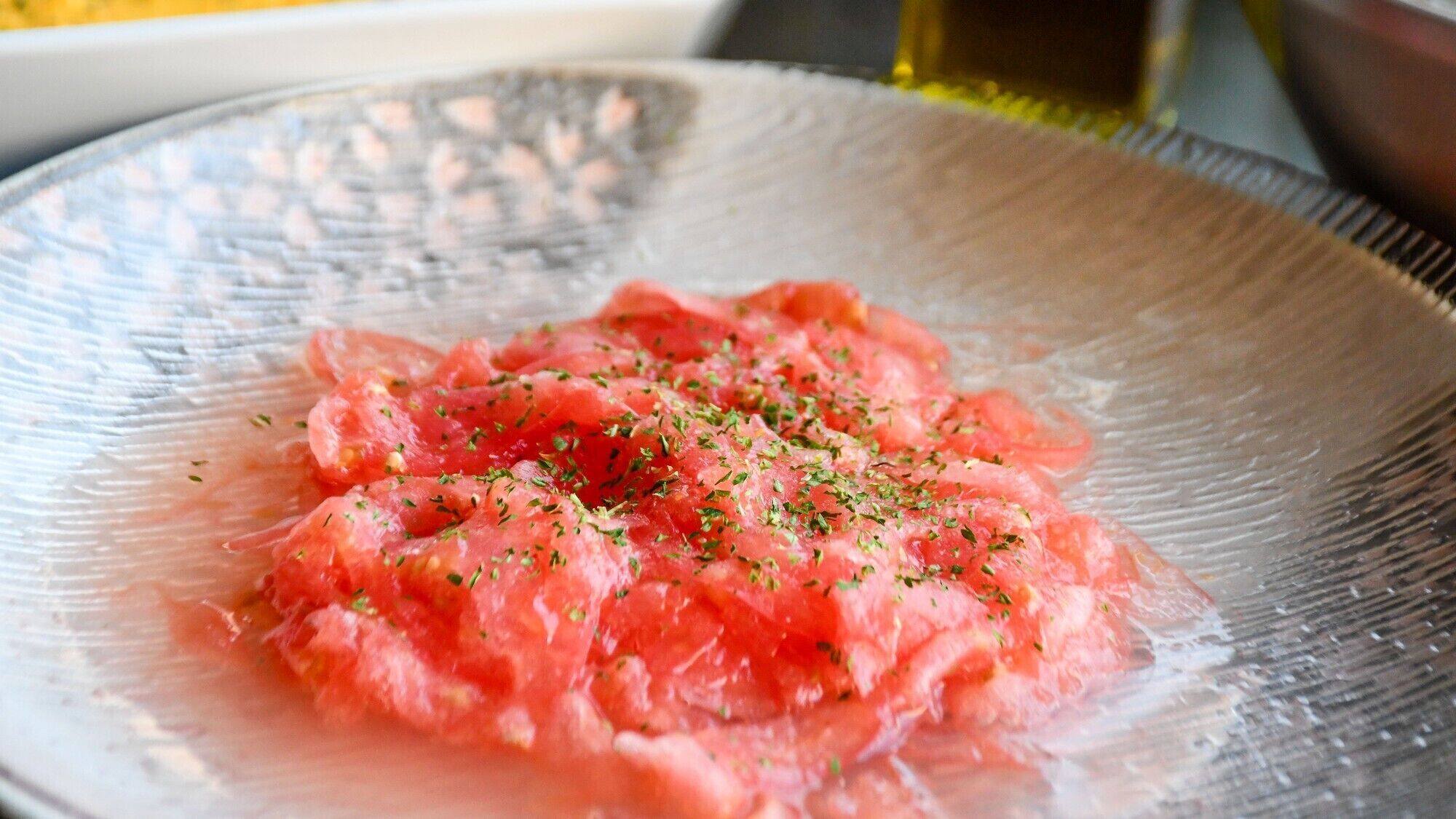 A clear glass bowl with a textured edge containing a pinkish food item, possibly a salad, garnished with green herbs.