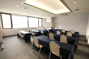 Un salón de conferencias con mesas y sillas, ventanas amplias, una pizarra y un reloj en la pared.