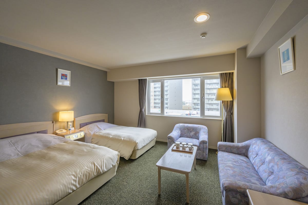 A hotel room with two beds, a small table, a chair, and a sofa.