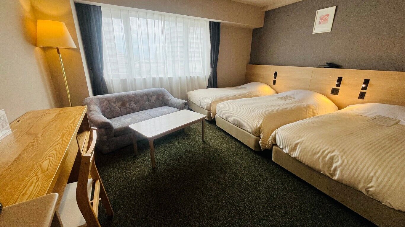 Een hotelkamer met twee bedden, een bank, een houten tafel en een lamp.