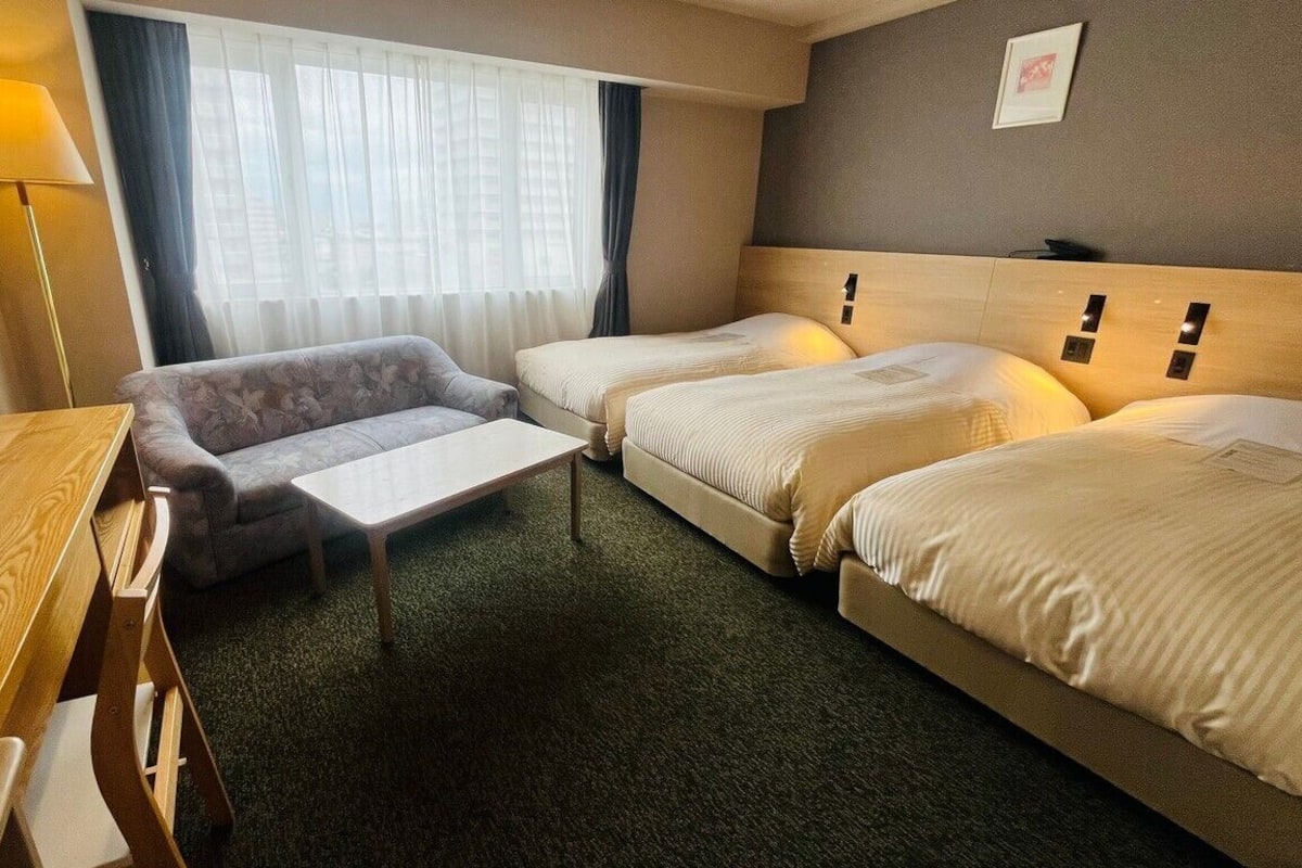 A hotel room with two beds, a sofa, a wooden table, and a lamp.