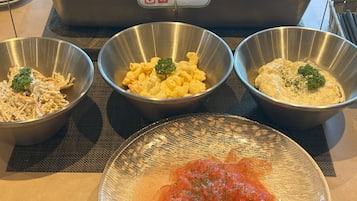 Three metal bowls on a table with a plate of tomato salad in front.
