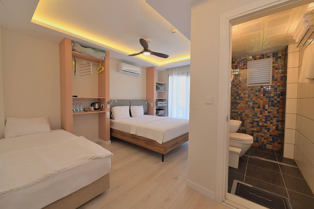 A hotel room with a bed, a desk, a wardrobe, an air conditioning unit, and a bathroom with a tiled shower wall.