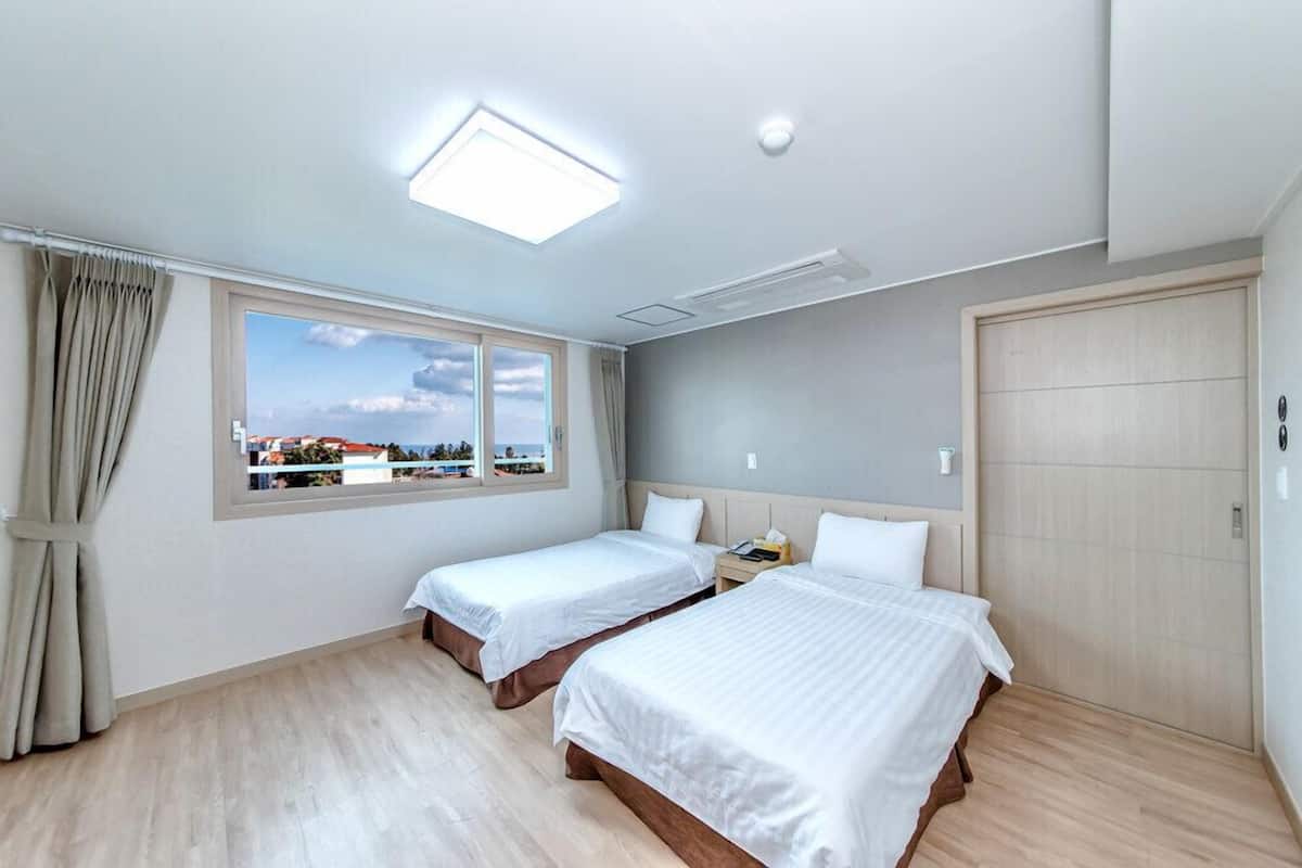 Une chambre d’hôtel avec deux lits, une grande fenêtre donnant sur la ville, un luminaire au plafond et une armoire en bois.