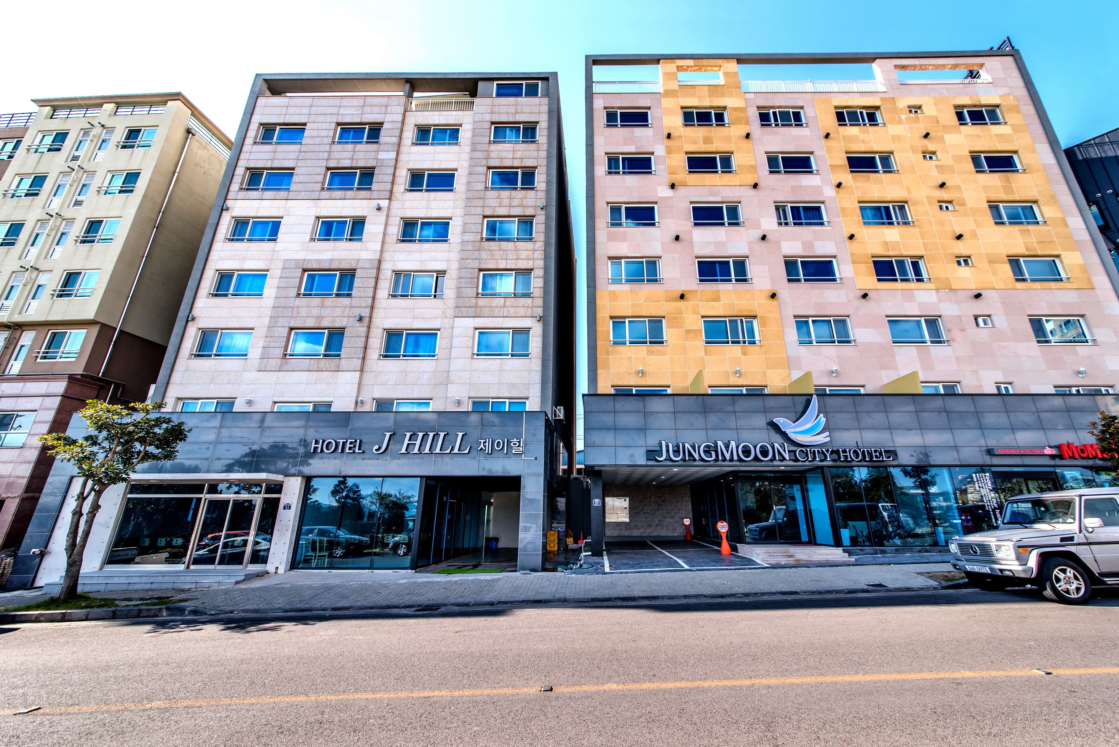 A modern hotel with a flat facade, large windows, and a parking lot in front.