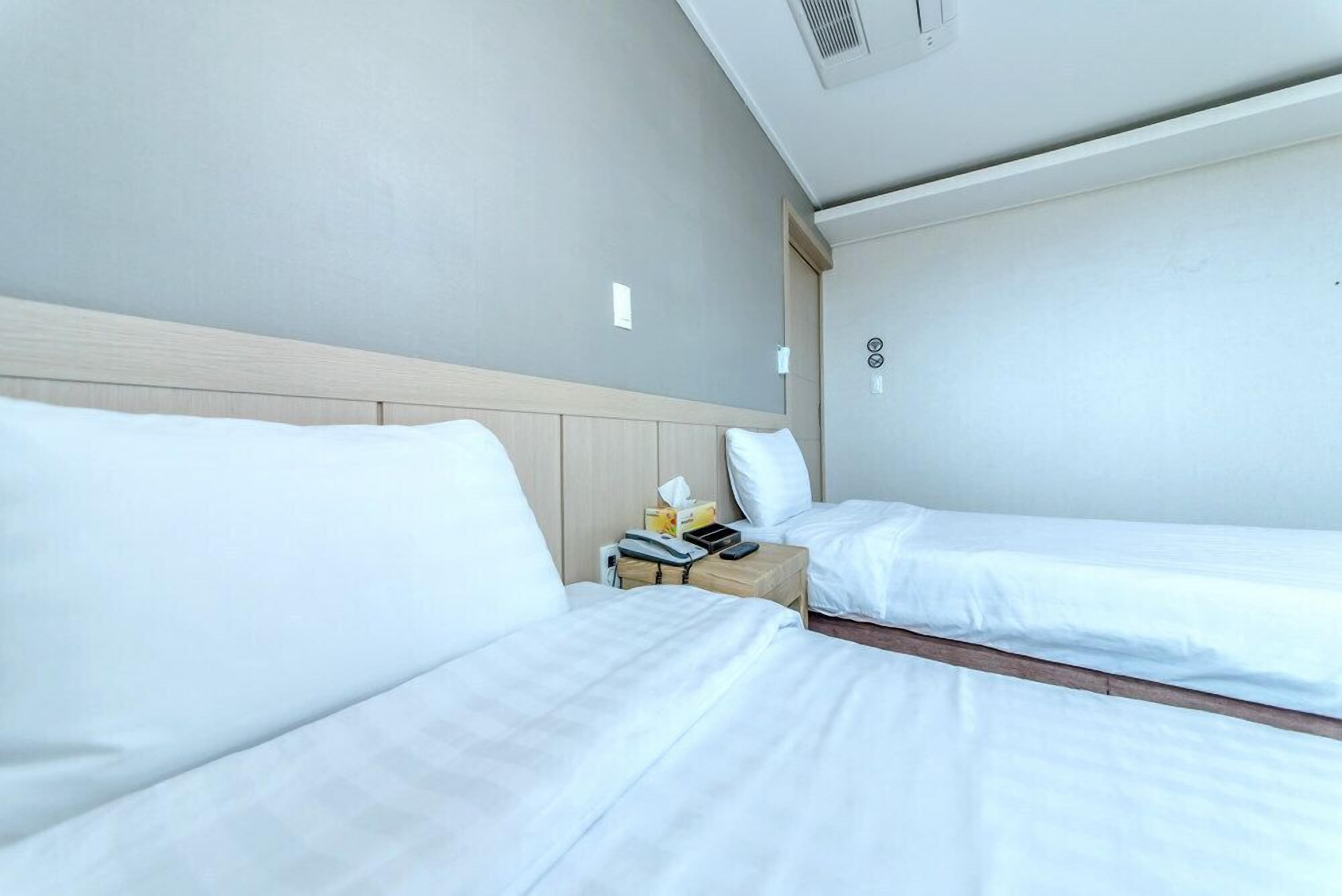 Una habitación de hotel con dos camas individuales, un cabecero de madera, una mesita de noche con lámpara y un pequeño atril.