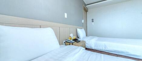 Una habitación de hotel con dos camas individuales, un cabecero de madera, una mesita de noche con lámpara y un pequeño atril.