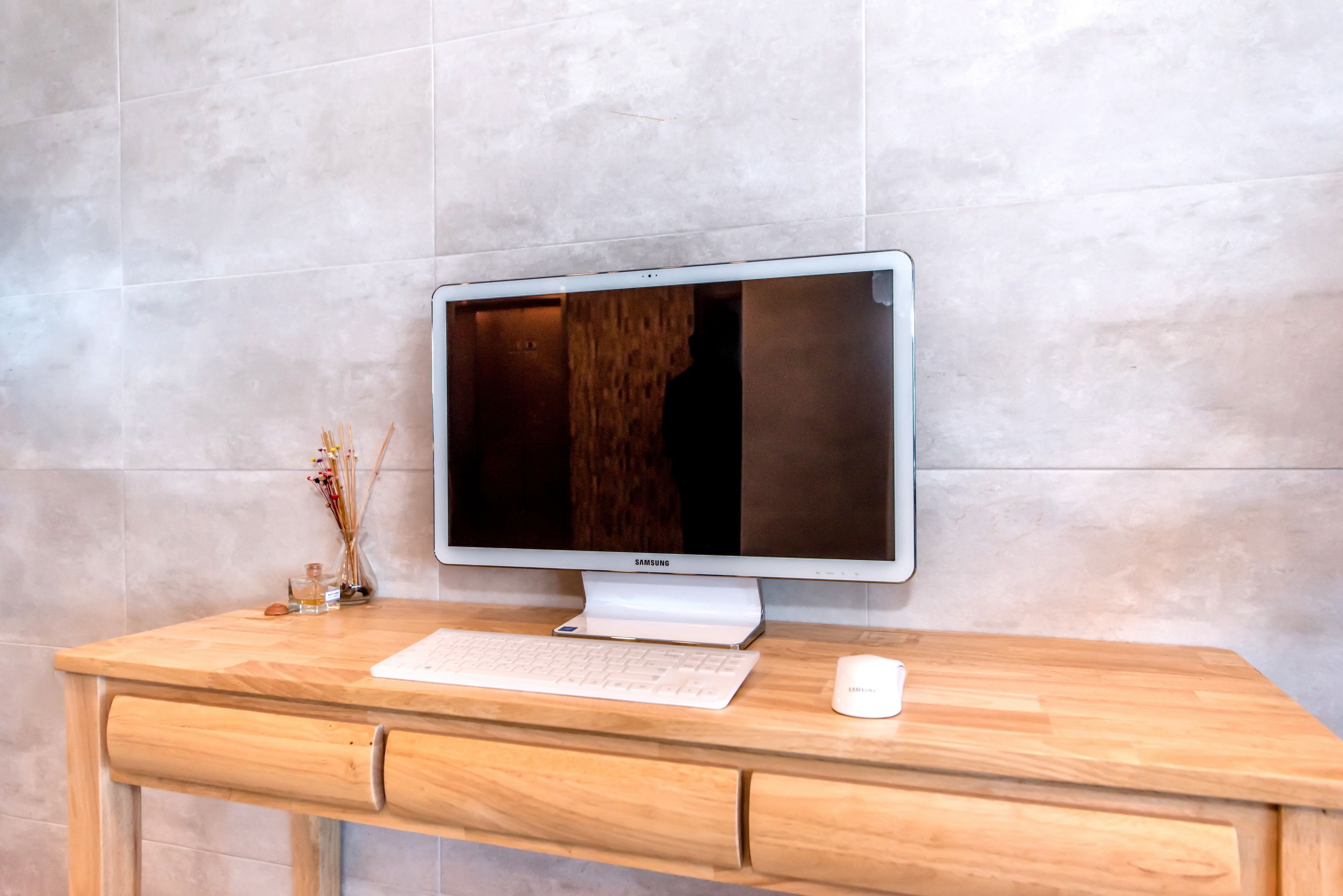 A wooden desk with a Samsung monitor, keyboard, and a white mug.