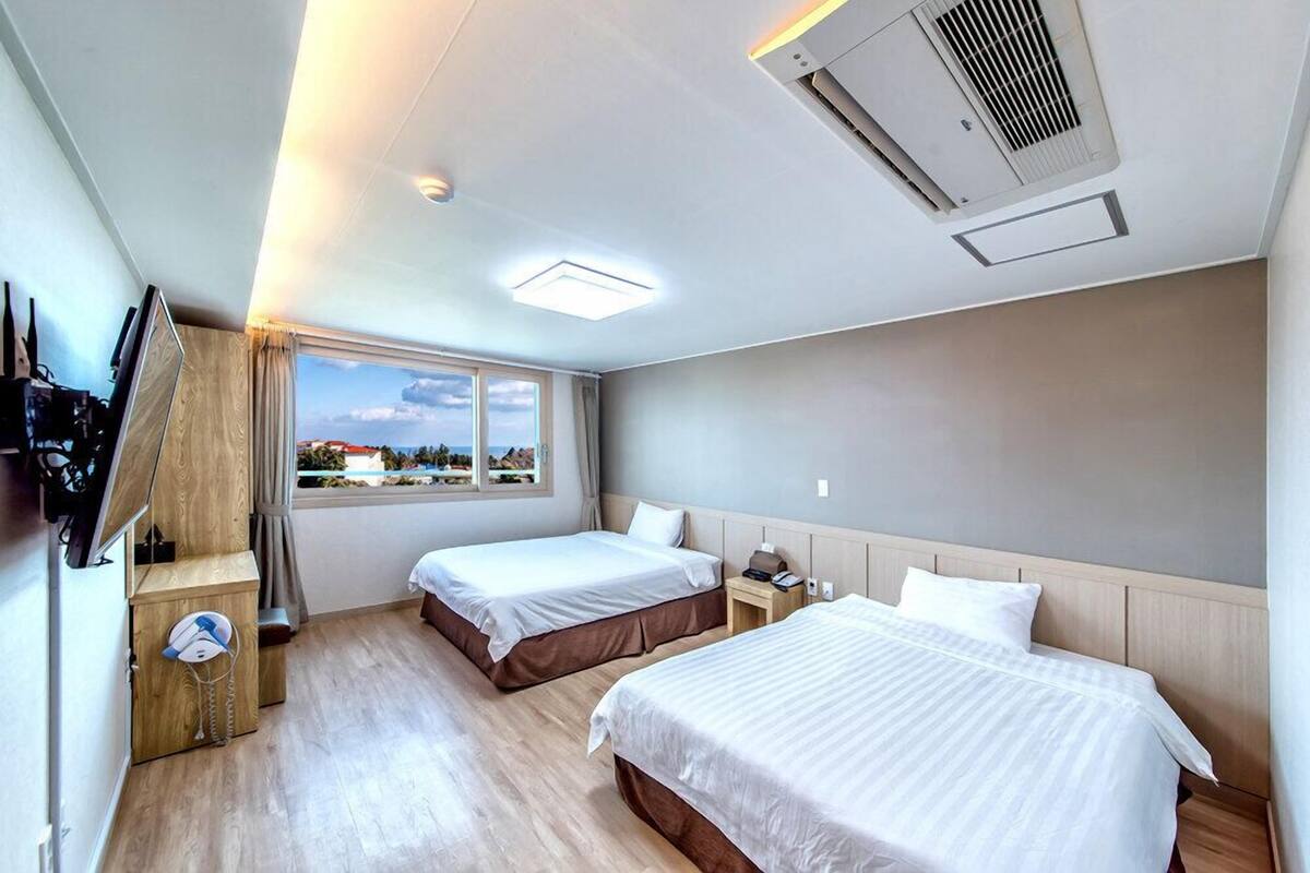 Une chambre d’hôtel avec deux lits, une fenêtre donnant sur un beau paysage, un bureau avec une lampe et un appareil de climatisation.