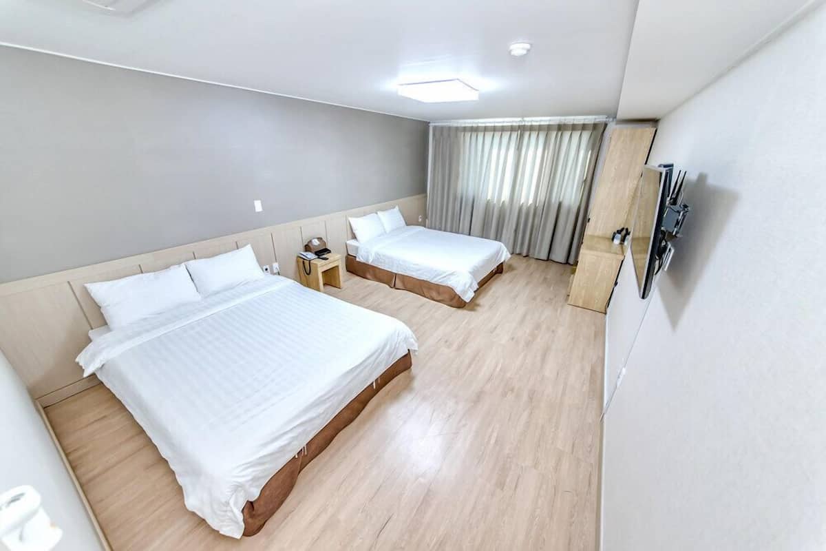 Une chambre d’hôtel avec deux lits, un bureau, une chaise, une télévision et une fenêtre avec des rideaux.