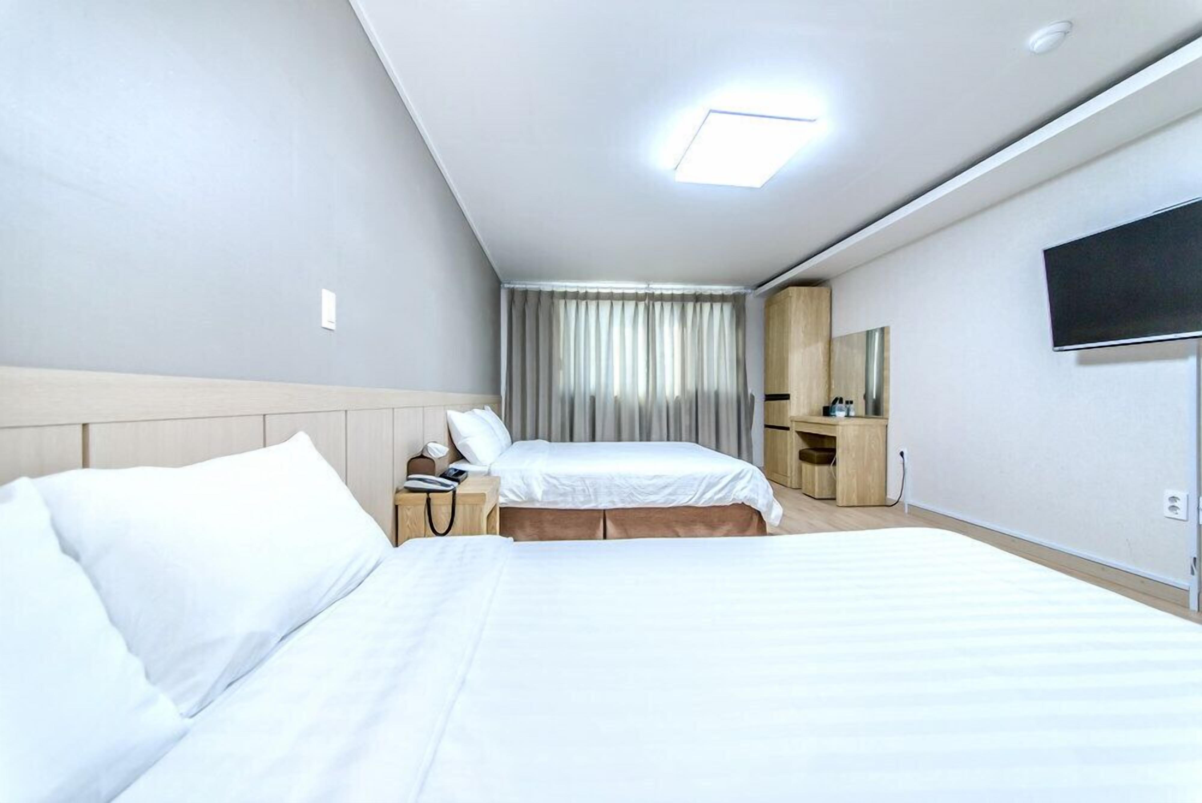 A hotel room with two beds, a desk, a chair, a TV, and a window with curtains.